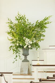 a vase filled with white flowers on top of a wooden table next to pews