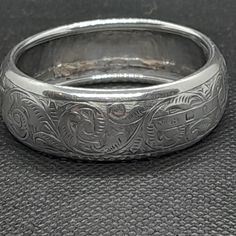 a silver wedding band with an intricate design on the outside and inside, sitting on a black leather surface