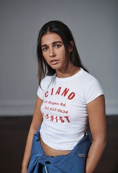 a woman in a white shirt is holding a blue bag and looking at the camera