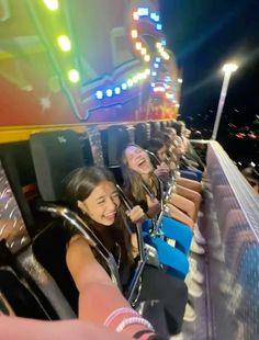 two girls are riding on a roller coaster at night with their hands in the air