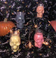 four jars with skulls and candles in them on a black cloth covered tablecloth, decorated with halloween decorations