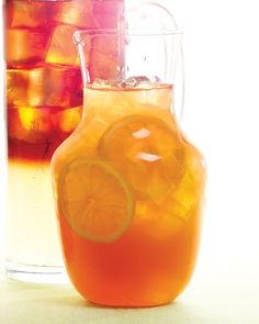 a pitcher filled with orange juice next to a glass full of ice and lemon slices