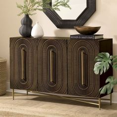 a sideboard with two vases on top of it next to a mirror and potted plant