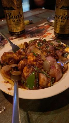 a white plate topped with meat and veggies next to two bottles of beer