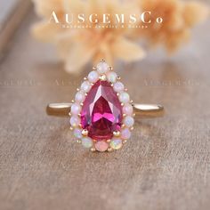 a close up of a ring with a pink stone and pearls on the bottom, surrounded by flowers