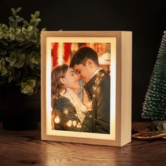 a wooden photo frame with lights around it on a table next to a christmas tree