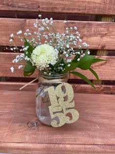 a mason jar filled with white flowers on top of a wooden table next to a bench