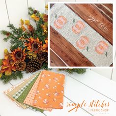 an orange and white quilted table runner with pumpkins on it, next to pine cones and flowers