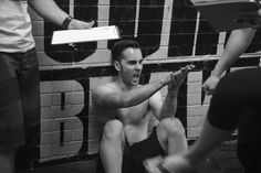 a shirtless man sitting on the ground in front of a brick wall with other people