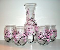 four wine glasses and a vase with pink flowers painted on the glass are sitting next to each other