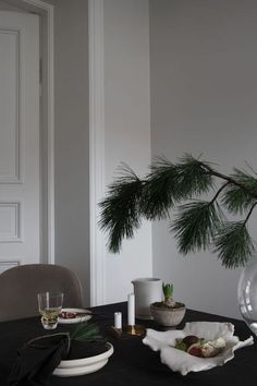 a dining room table with plates and bowls on it, pine branches in the background