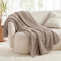 a white couch covered in a blanket on top of a shaggy rug next to a potted plant