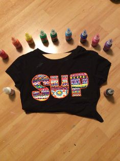 a black shirt with the word sup on it surrounded by colored crayons