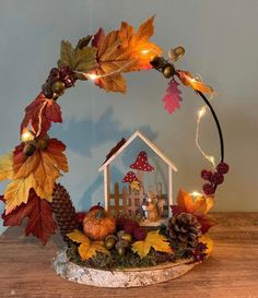 a small white house surrounded by autumn leaves and pine cones with fairy lights on the roof