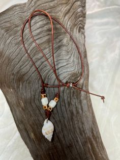 a necklace with two white beads and brown leather cord on top of a piece of wood