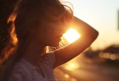 a woman standing in front of the sun with her hands on her head and arms behind her back