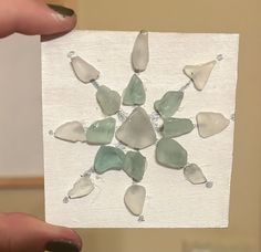 a person holding up a piece of paper with sea glass pieces on it in their hands