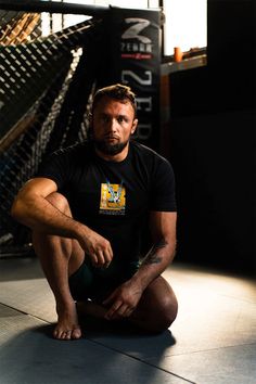 a man sitting on the ground with his legs crossed in front of him, wearing a black shirt and green shorts