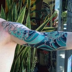 a man's arm covered in blue and white ink with an ocean wave on it