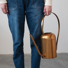 a woman holding a metal watering can in her hands and wearing blue jeans with white shoes