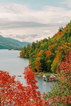 a lake surrounded by trees with red leaves in the foreground and mountains in the background