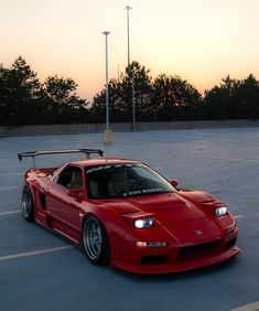 a red sports car is parked in a parking lot at sunset with trees in the background