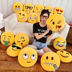 a woman sitting on the floor surrounded by many emotictive smiley face pillows,