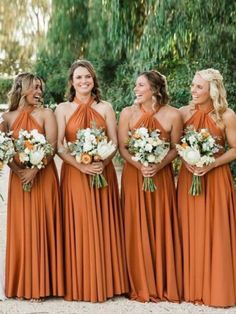 a group of women standing next to each other wearing orange dresses and holding bouquets