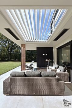 an outdoor living area with couches and chairs under a roof that is open to the backyard