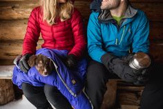 a man and woman sitting next to each other with a dog wrapped in a blanket