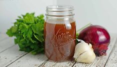 a mason jar filled with liquid next to some vegetables on a wooden table, including celery and onions