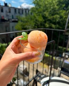 a person holding up a small glass filled with fruit on top of a balcony railing