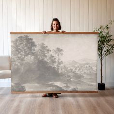 a woman holding up a large painting in front of her face