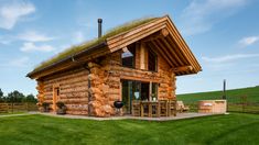 a small log cabin with grass on the roof and patio area in front of it