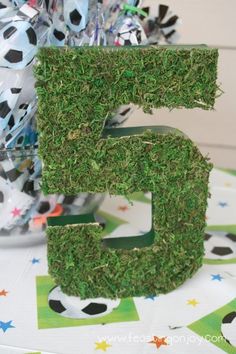 the number five is made out of grass and sits on a table with soccer balls