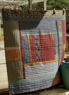 an old quilt hanging on a clothes line with a potted plant in the foreground