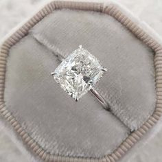 a cushion - cut diamond ring sits on top of a gray velvet pillow in an elegant setting