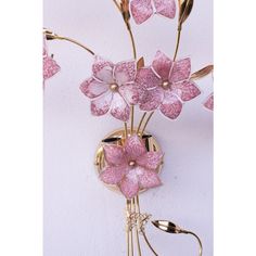 pink flowers are in a gold vase on a white wall and hang from the hooks