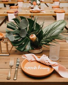 a table set for an event with place settings and greenery