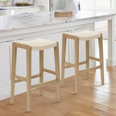 two wooden stools sitting in front of a white counter top on a hard wood floor