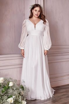 a woman in a white dress standing on a wooden floor next to flowers and greenery