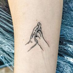 two hands holding each other on the wrist tattoo design by person's arm with blue water in background