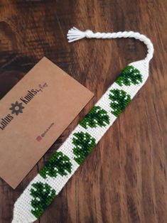 a white and green beaded bracelet on a wooden table next to a box with a card