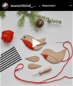 some wooden birds and needles on a white table with red thread, pine cones and balls of yarn