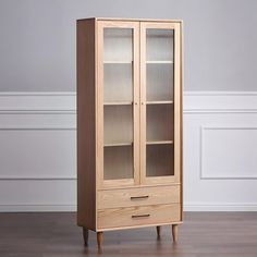 a tall wooden cabinet with glass doors on the top and bottom drawers, in front of a white wall