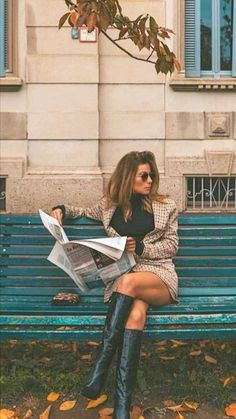 a woman is sitting on a bench reading the paper while holding her leg up to her knee