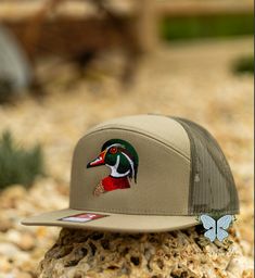 Show off your love for the great outdoors with our Wood/Woody Duck Embroidered Richardson 168 Hat/Cap. The intricate stitching of the duck design adds a touch of rustic charm, while the Richardson 168 hat/cap provides comfort and durability for all your outdoor adventures. Embrace your passion for nature and style with this one-of-a-kind hat/cap. 60/40 cotton/polyester100% polyester mesh backStructured, six-panel, mid pro profilePre-curved billAdjustable plastic snapback This is a physical produ Outdoor Fall Snapback Hat, Country Style Trucker Hat With Curved Brim For Outdoor, Fall Outdoor Snapback Hat, Rustic Outdoor Cap, Embroidered Adjustable Trucker Hat For Outdoor, Country Style Baseball Cap For Outdoor, Country Style Snapback Hat With Curved Brim For Outdoor, Khaki Hats For Outdoor Fall Use, Khaki Outdoor Hat For Fall