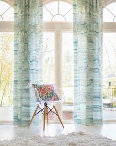 a chair sitting on top of a white rug in front of two windows with blue drapes