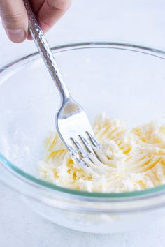 a person holding a fork in a glass bowl filled with whipped cream and other ingredients