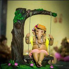 an elephant figurine sitting on a swing next to a tree